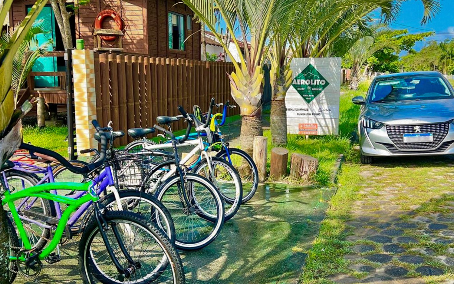 Bicicletas disponíveis para aluguel na Aerolito, encostadas na varanda entre as palmeiras