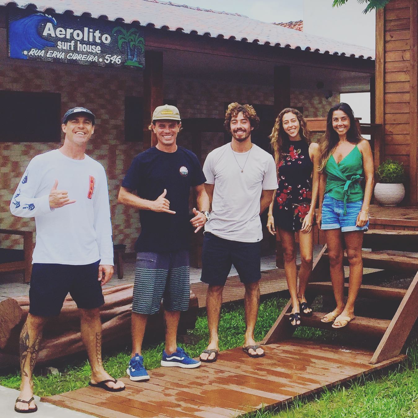 Yago Dora e amigos em frente à placa da Aerolito Surf House, Rua Erva Cidreira 546